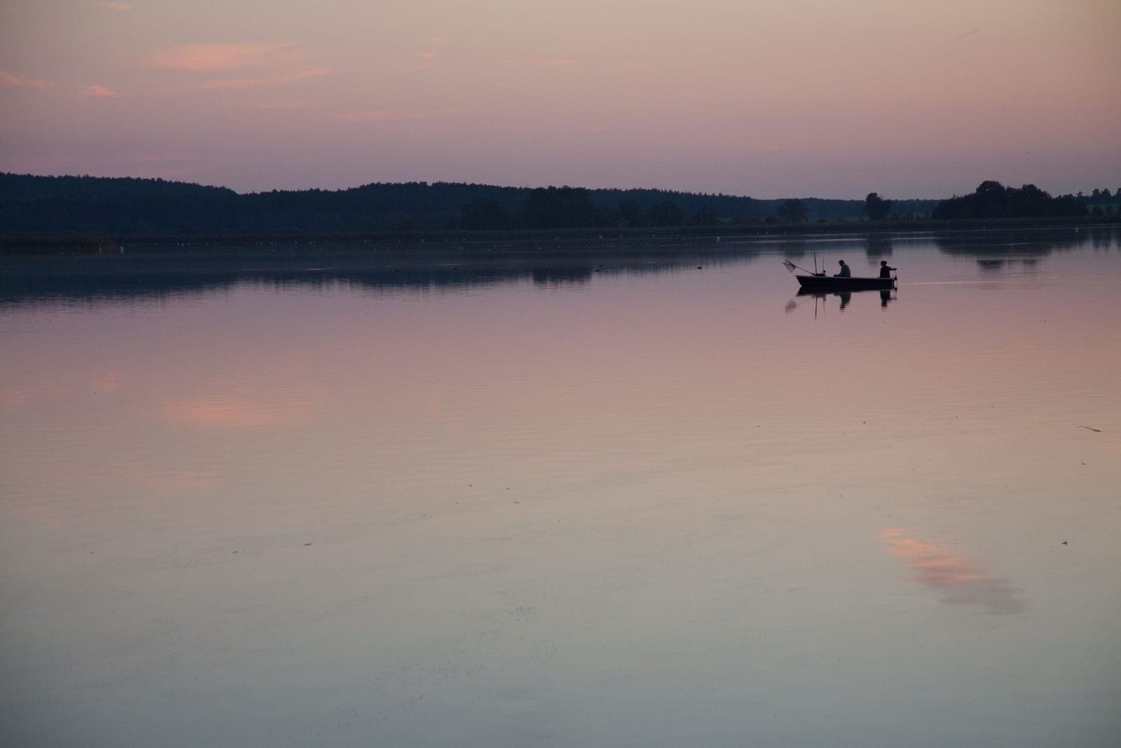 A loaded open boat on flat water at the edge of a lake