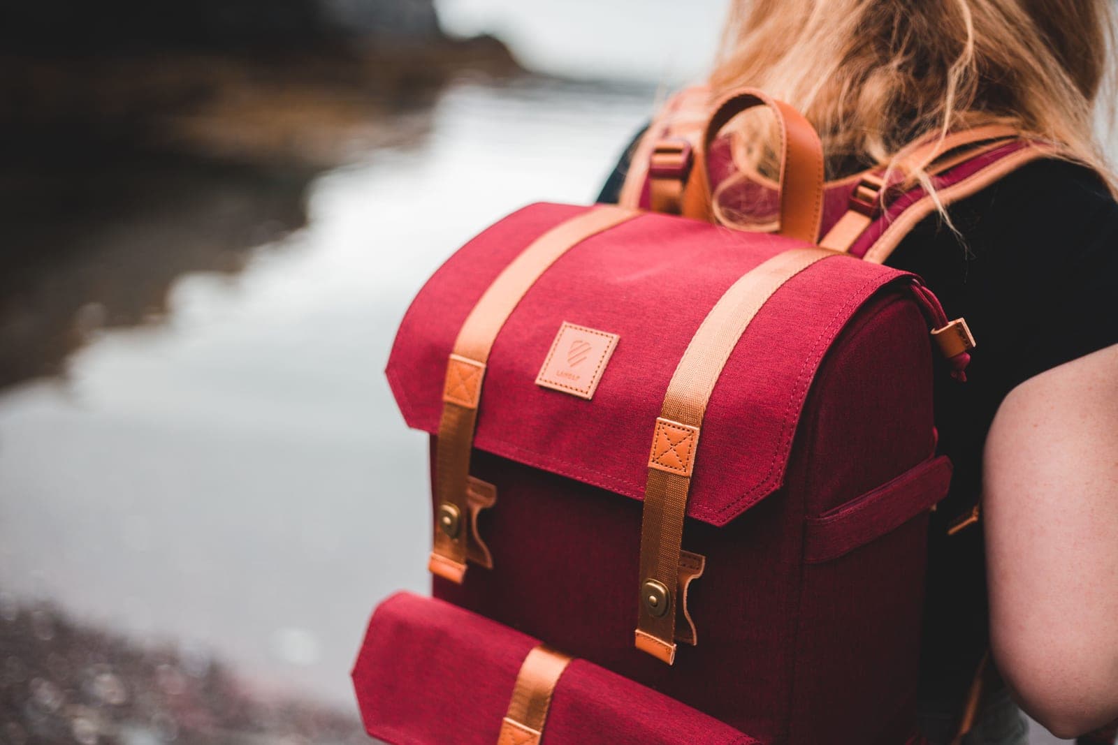 A person carrying a packed backpack down to a quiet lakeside