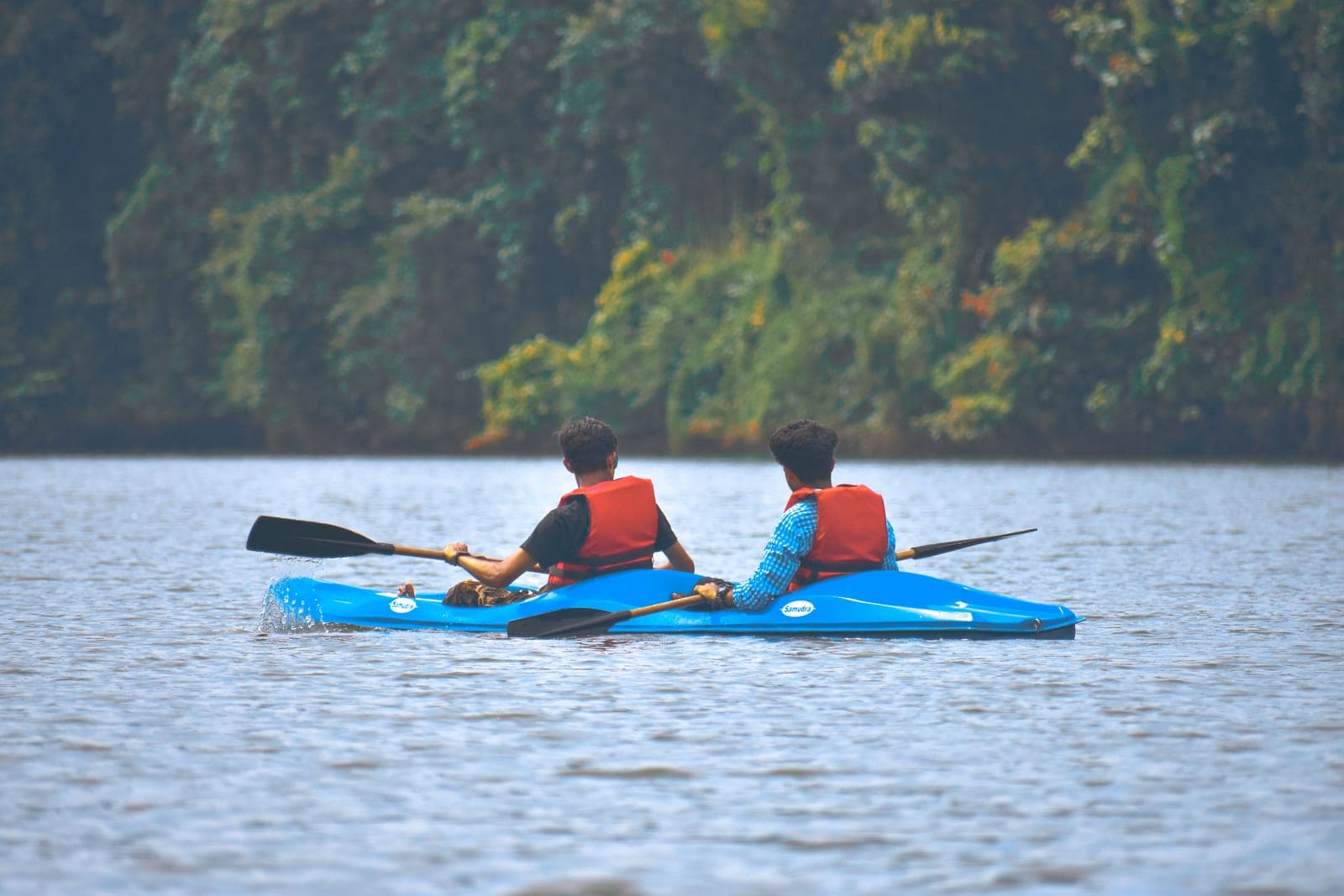 Two paddlers in a kayak on a calm river lined with greenery