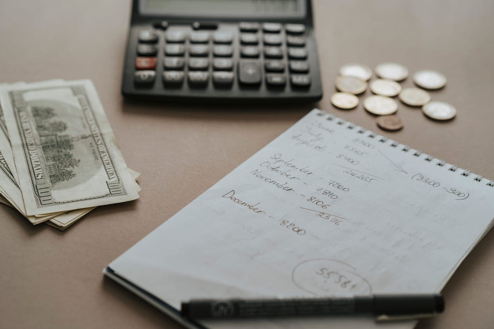 A notebook of handwritten calculations beside a pen