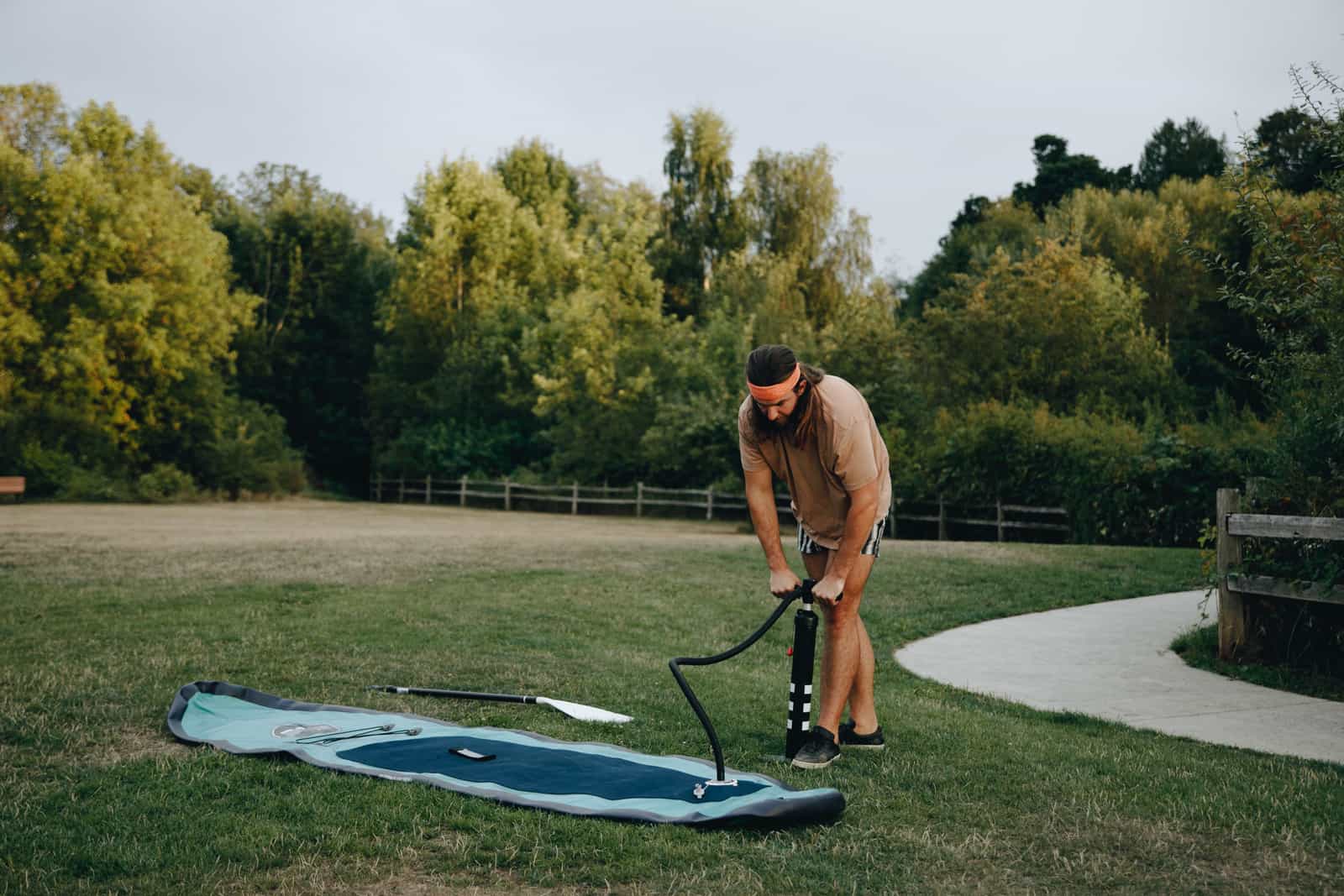 A person inflating a stand up paddle board with a pump on the grass