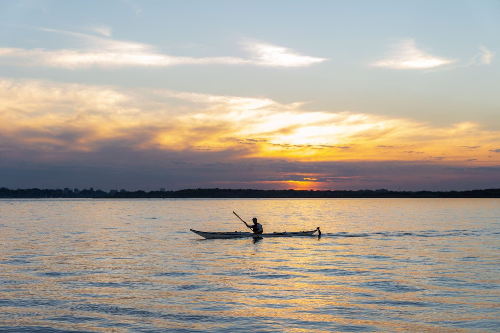 A lone paddler silhouetted on calm open water at sunset