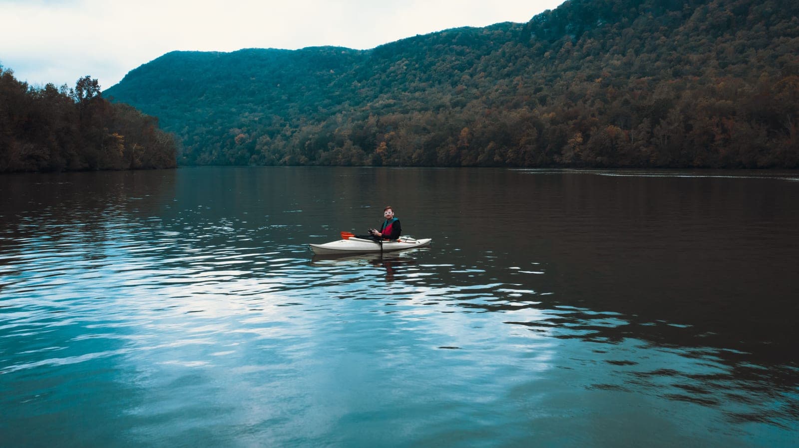 A kayaker on a calm open lake with mountains behind