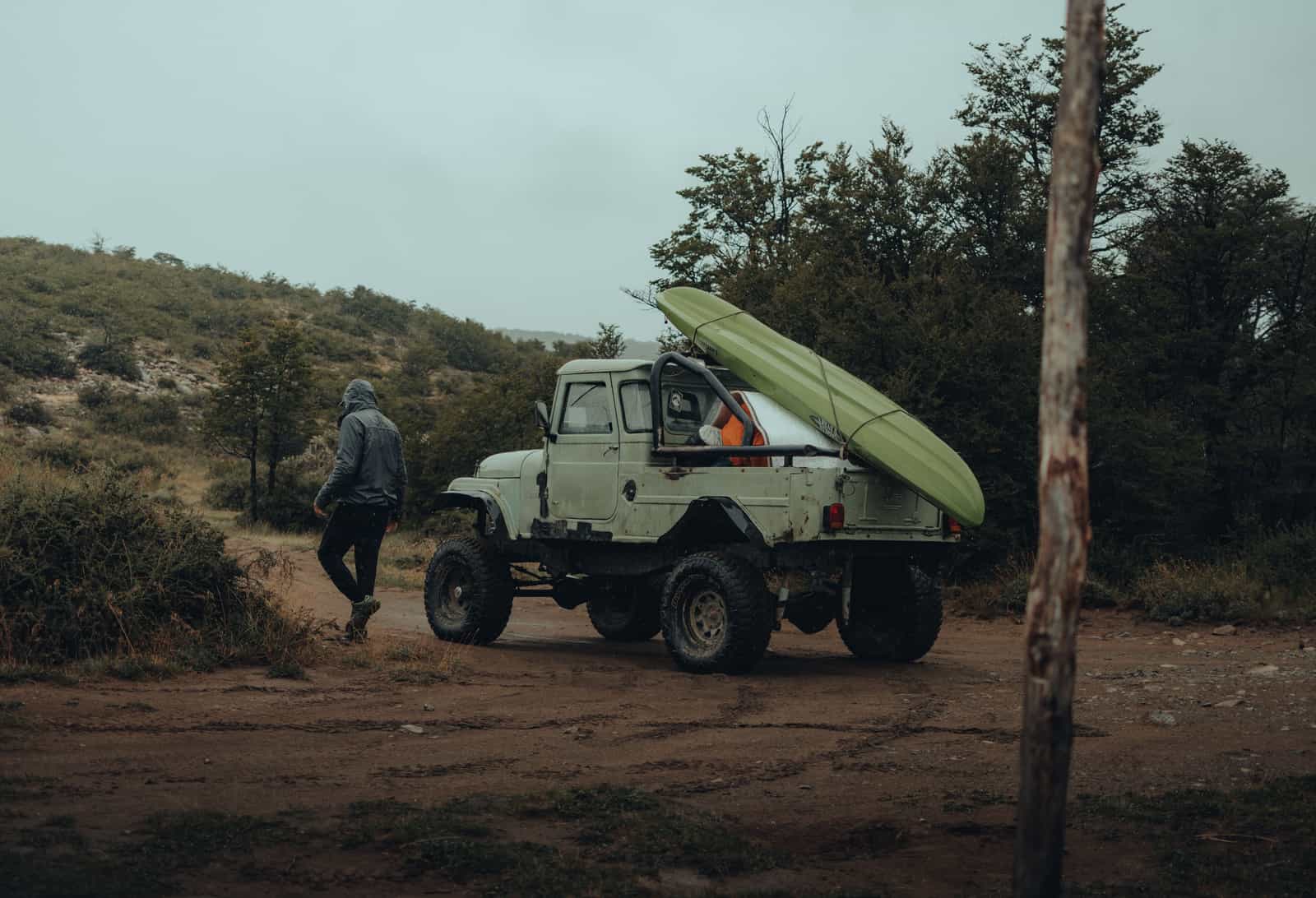 A packed kayak bag being carried away from a parked car