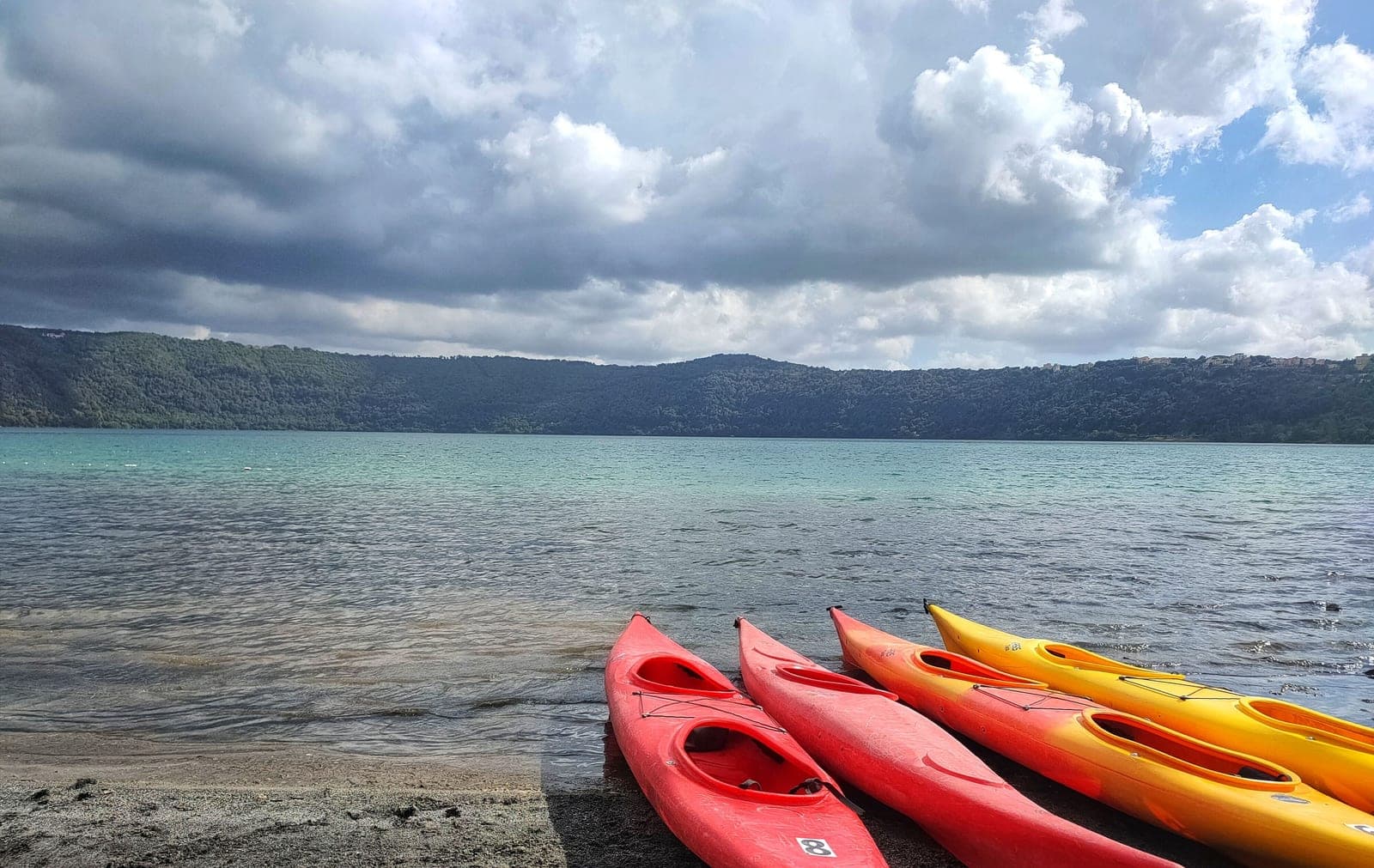 Kayaks lined up on a lake shore under a cloudy sky