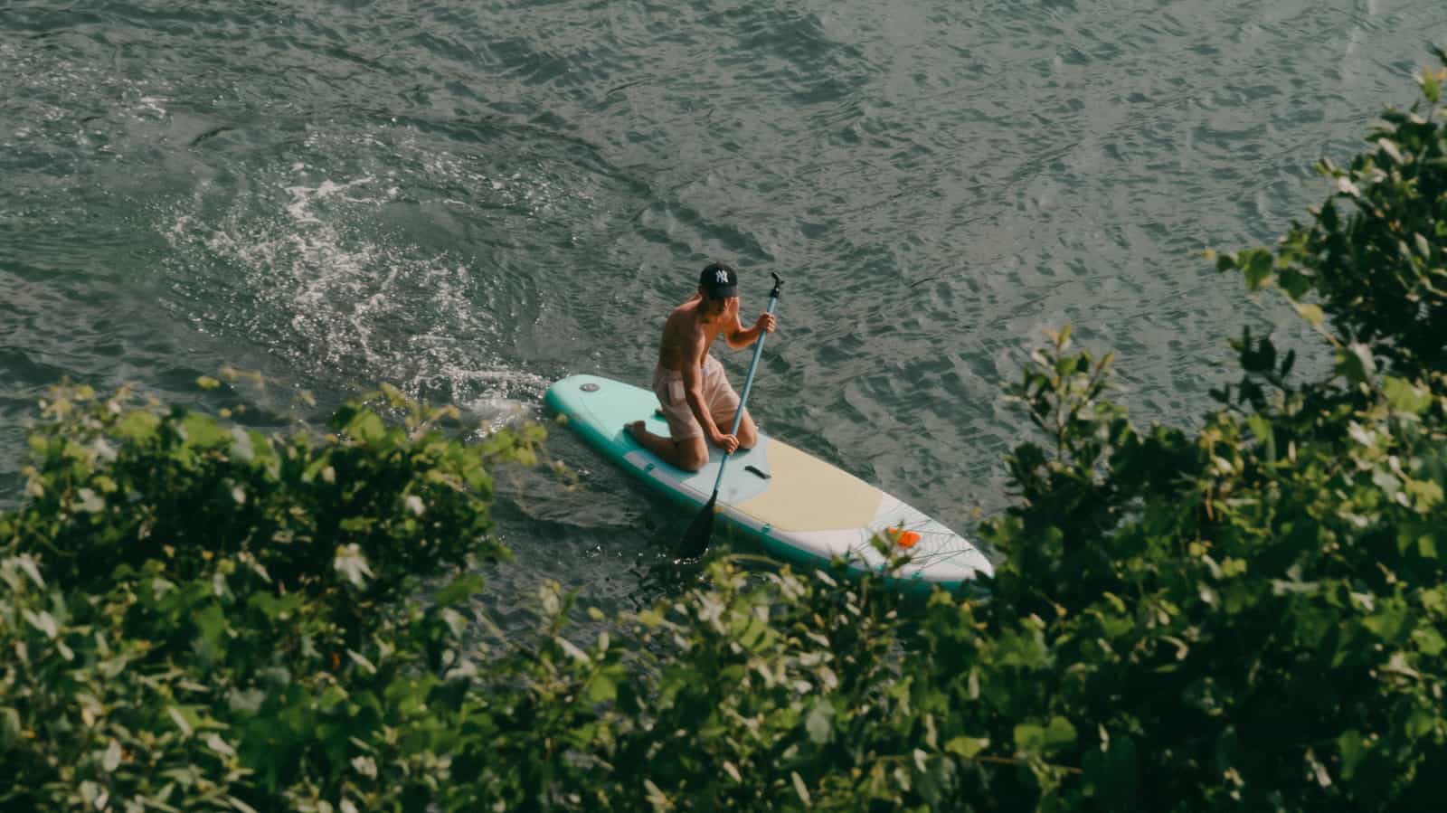 A paddle board packed into a backpack by the water
