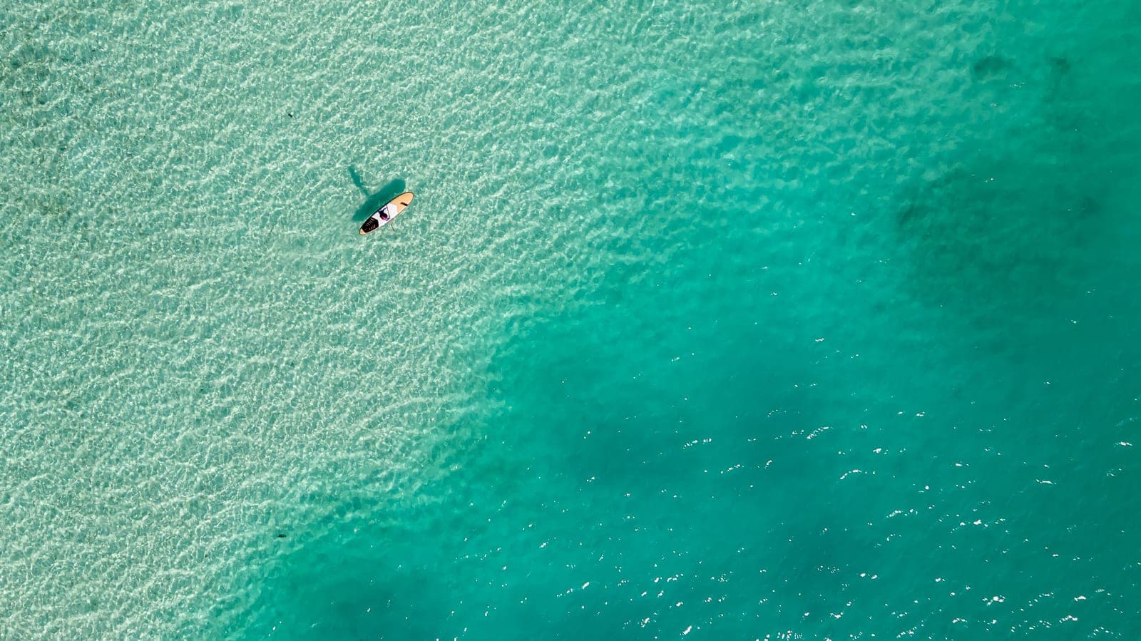Overhead view of a paddler on a board crossing clear shallow turquoise water